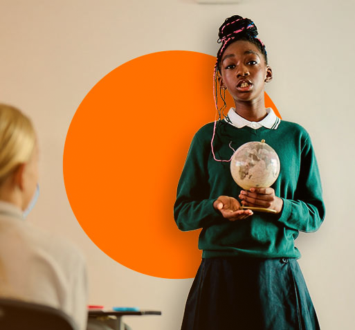 A young secondary girl standing in front of a class wearing her green school uniform and holding a small globe.