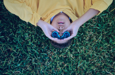 A kid laying in the grass holding binoculars.