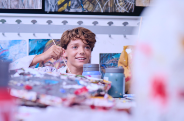 A primary student smiles while holding a paintbrush in art class.